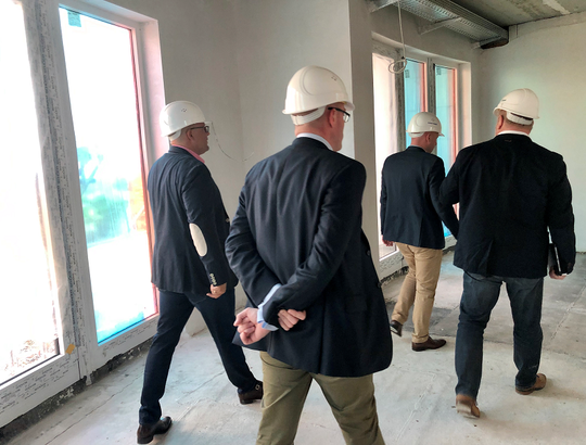 Vier Männer mit Schutzhelmen bei der Besichtigung des Rohbaus für ein neues Serviced Apartment